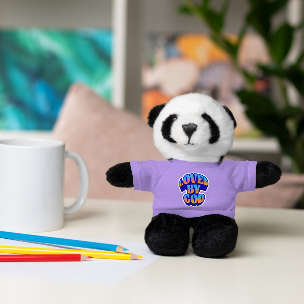 Plush panda bear wearing a purple "Loved by God" shirt sitting on a desk near pencils and a mug.