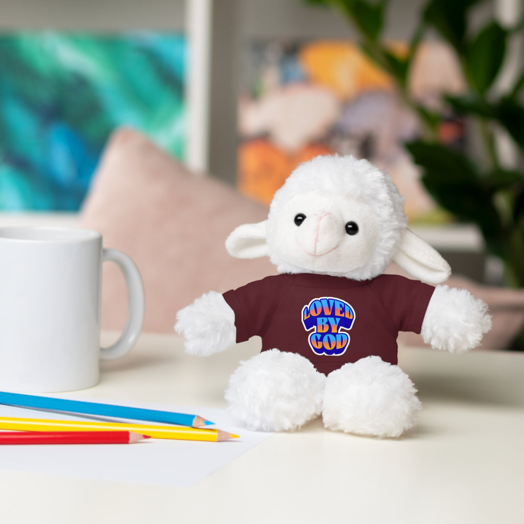 Plush white lamb wearing a maroon shirt with loved by God text sitting on a desk with pencils and mug nearby